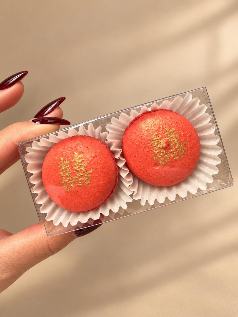 Two red macarons with gold double-happiness characters in a clear favor box