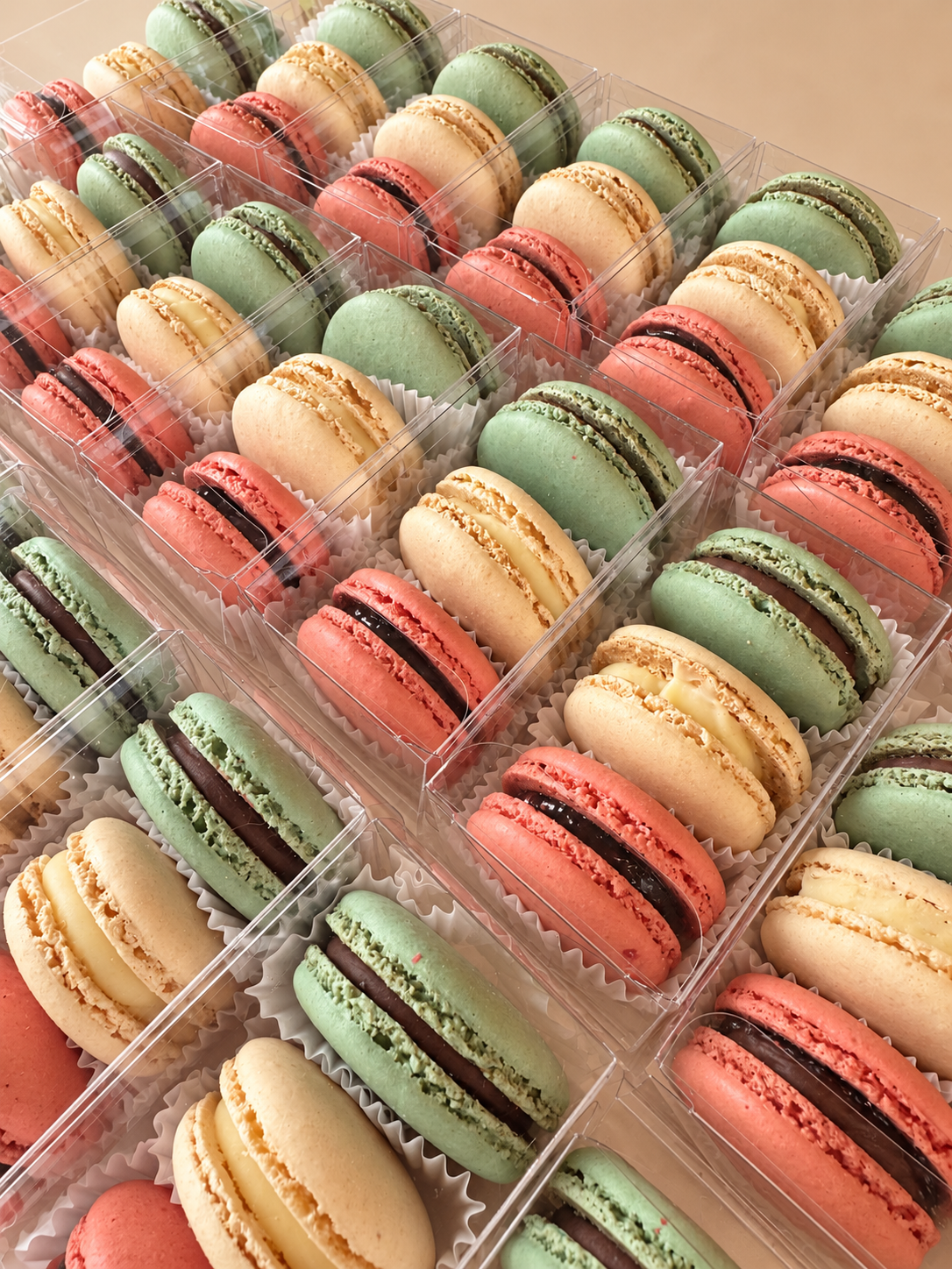 Rows of clear three-piece macaron favor boxes in pink, vanilla and green