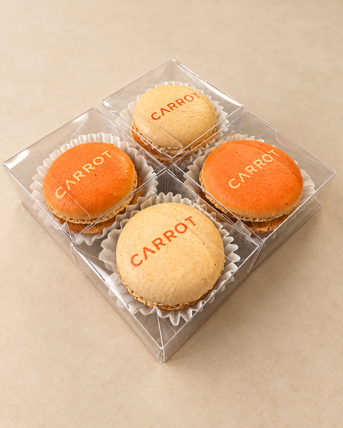 Four clear boxes of orange and peach macarons printed with the Carrot logo on a blue background