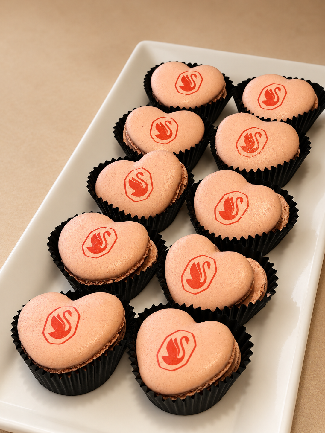 Heart-shaped peach macarons printed with the red Swarovski swan logo in black paper cups