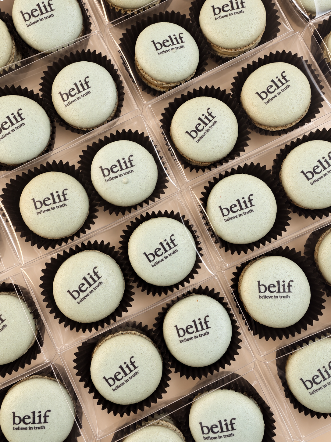 Ivory macarons printed with the belif logo in black cups inside clear favor boxes