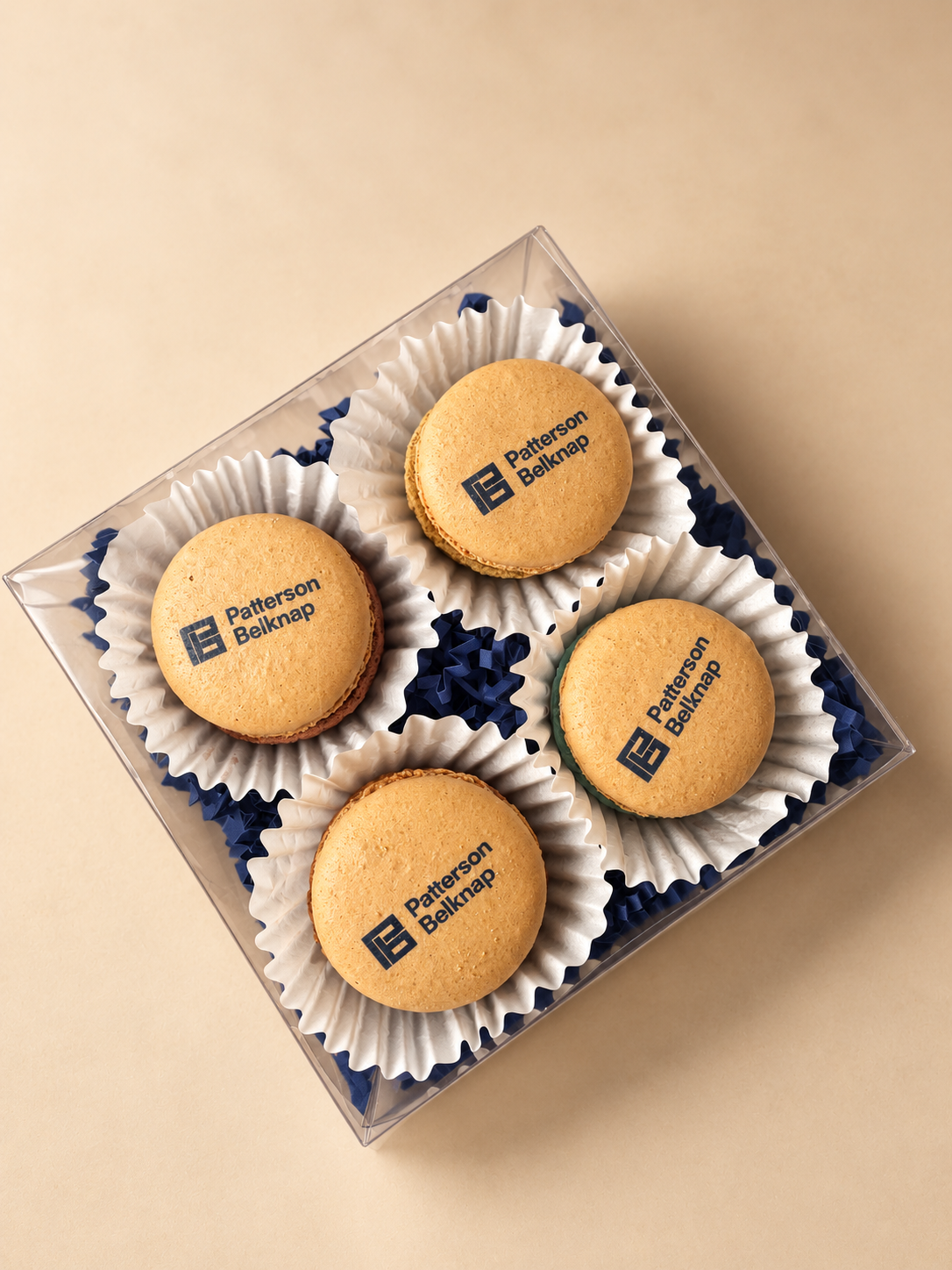 Four macarons printed with the Patterson Belknap logo in a clear box on a blue background