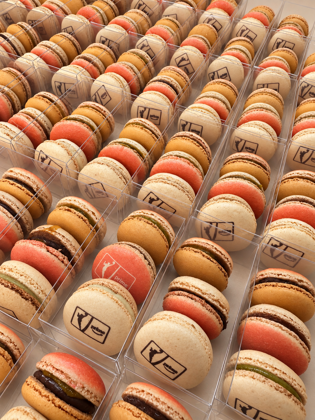 Clear boxes of orange, coral and natural macarons, many printed with the WNBA and Prime Video logos