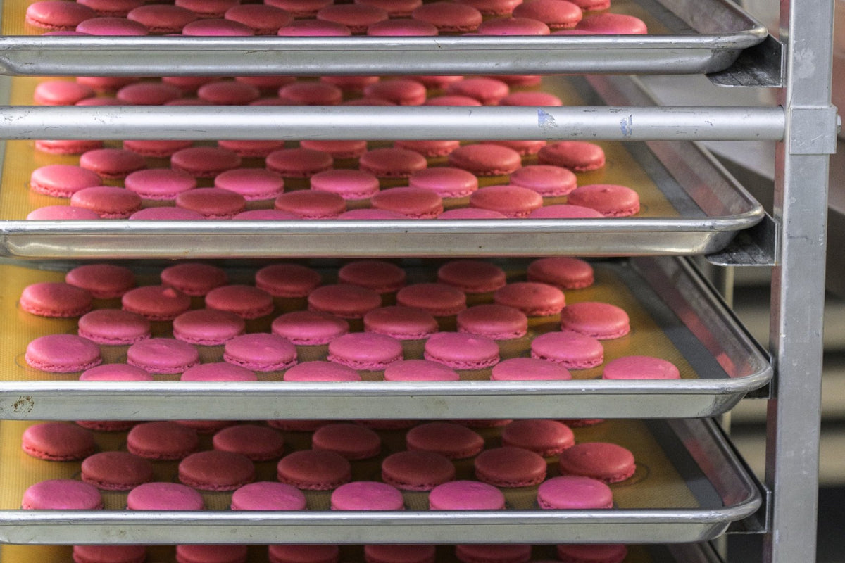 Rack of baked pink macaron shells cooling on sheet trays
