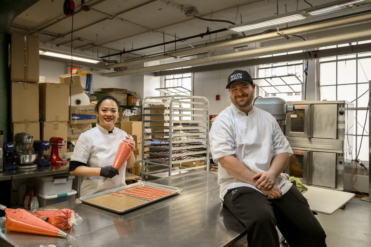 BKLYN MACS co-founders Rebecca and Gene in their production kitchen, with a tray of freshly piped macaron shells