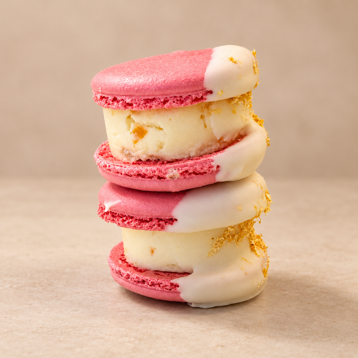 Two stacked pink macaron sandwiches with a thick vanilla filling, half-dipped in white chocolate with gold flakes