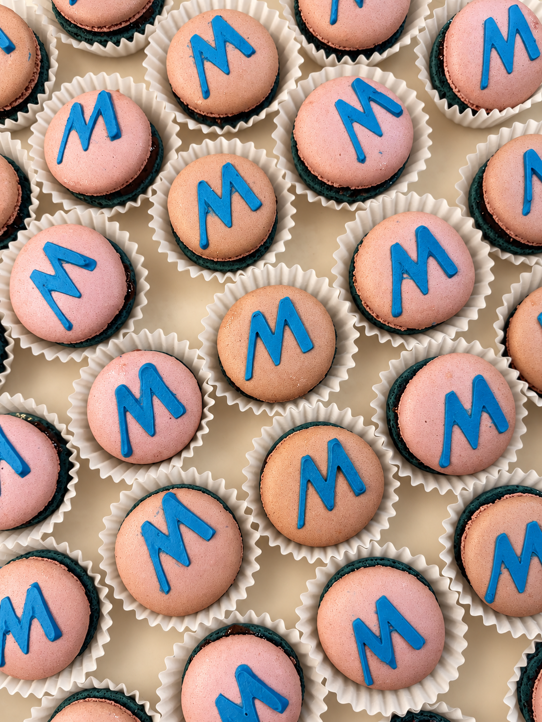 Rows of pink macarons, each topped with a raised, three-dimensional blue Marshalls M logo