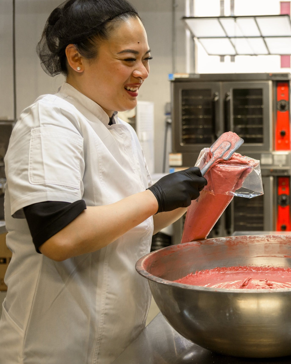 Rebecca smiling as she fills a piping bag with pink macaron batter