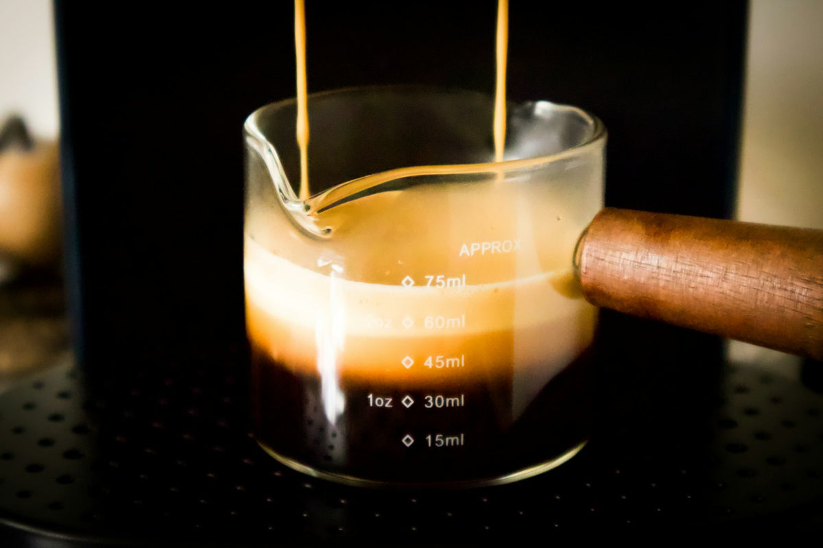 Espresso pouring from a machine into a glass shot pitcher