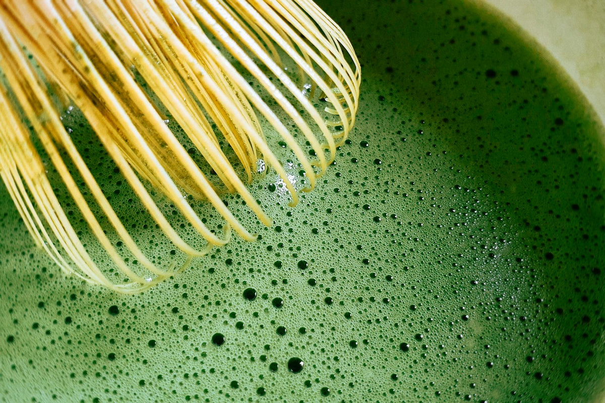 Bamboo whisk frothing bright green matcha in a bowl